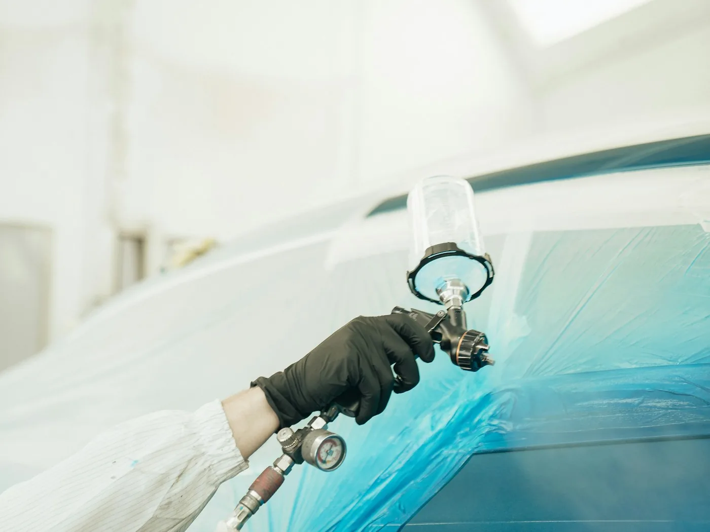 Lackierpistole beim Auftragen von Farbe auf ein abgeklebtes Fahrzeug